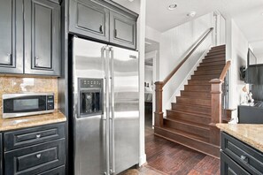A kitchen with a stainless steel refrigerator, a built-in microwave, and a water dispenser. There is a wooden staircase leading to another level.