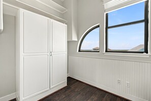 A room with a white wardrobe, a window with a view of the beach, and a white wall with a vent.