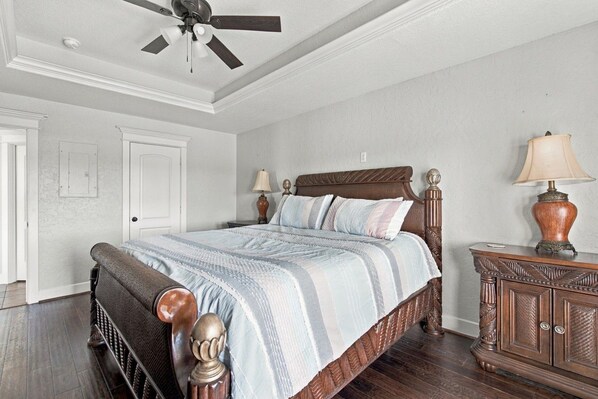 A bedroom with a bed, a ceiling fan, a nightstand with a lamp, and a wooden cabinet.