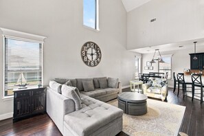 A spacious living room with a sectional sofa, a round coffee table, and a large wall clock.