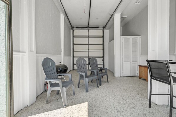 A room with a white door, a grill, and three Adirondack chairs.