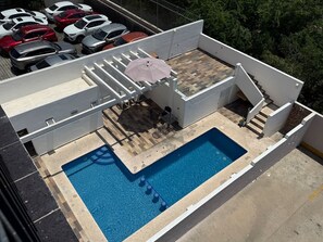 A rooftop swimming pool with a view of parked cars and trees. - Marina Suites | Vive la Marina de Mazatlán by GPS (Mazatlán)