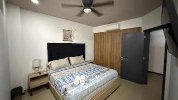 Une chambre à coucher comprenant un lit, une table de chevet, un ventilateur de plafond, une armoire et une porte.