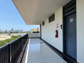 A corridor with a fire extinguisher, a door marked 305, and a view of a beach and cityscape. - Marina Suites | Vive la Marina de Mazatlán by GPS (Mazatlán)