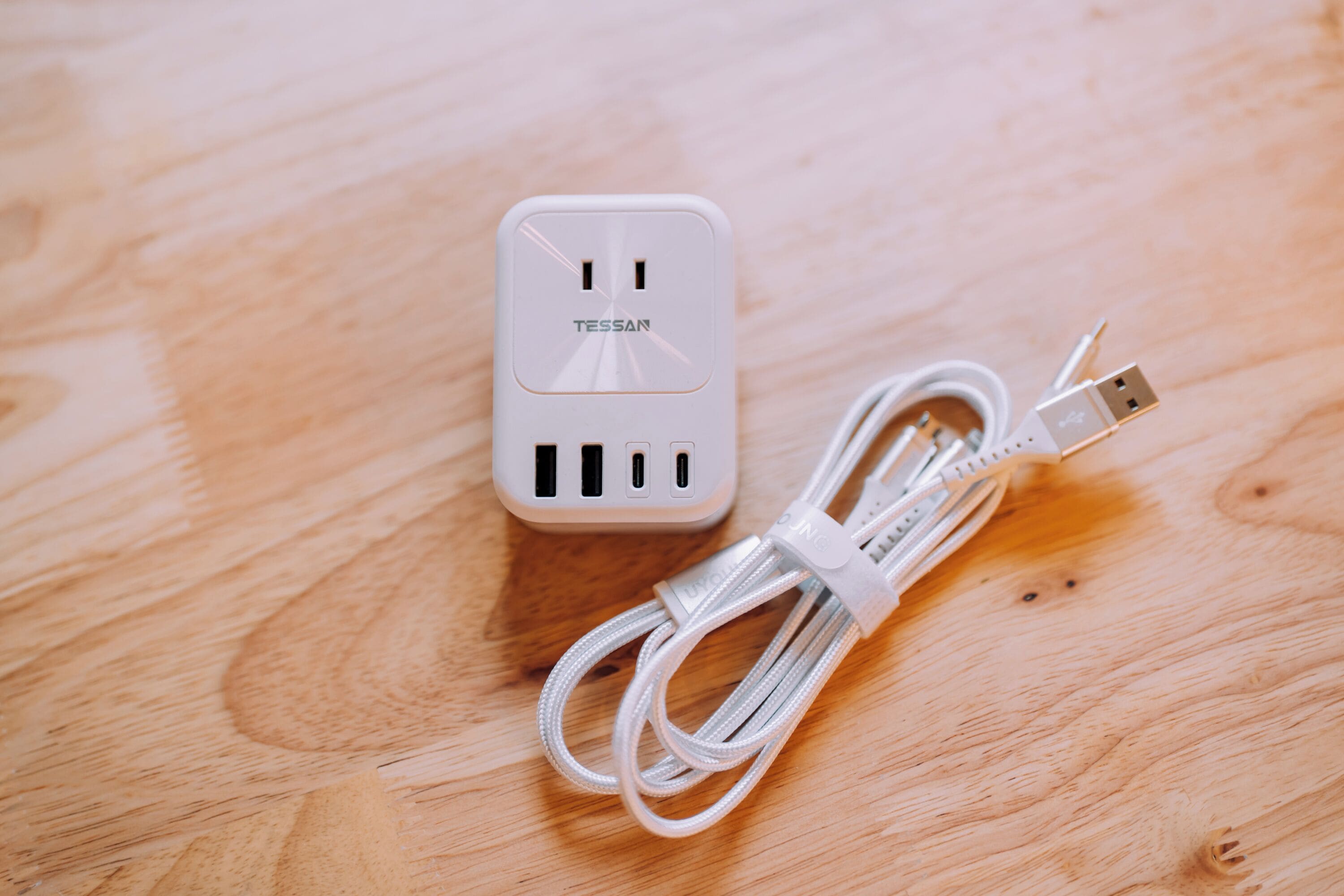 A white power strip with multiple USB ports and a cable on a wooden surface.