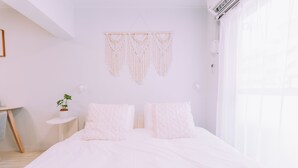 A bedroom with a bed, two pillows, a bedside table with a plant, and macramé wall hangings. - Maison de Tenjin Higashi 506 (Fukuoka)