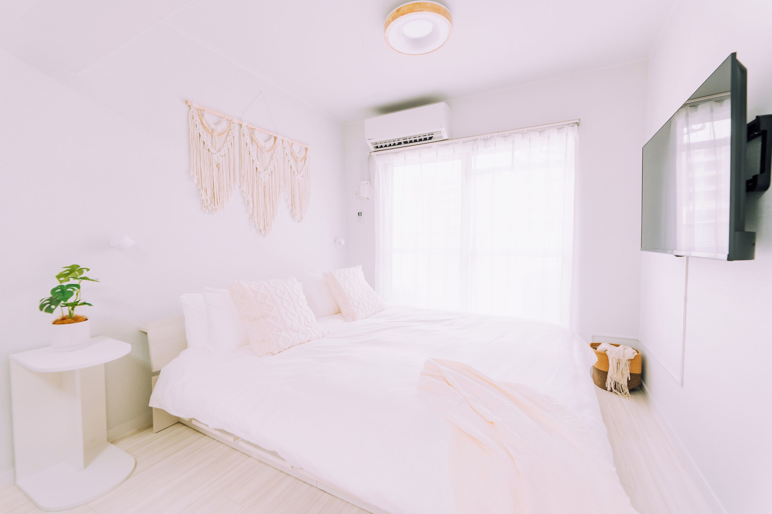 Une chambre à coucher au style minimaliste, avec un lit, une plante sur la table de chevet et une décoration murale en macramé.