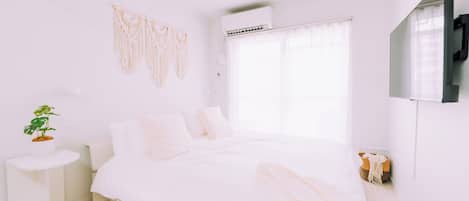 Un dormitorio minimalista con una cama, una planta en la mesita de noche y un colgador de macramé en la pared.