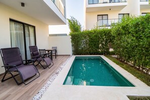 A swimming pool with a tiled deck, surrounded by a hedge and a building. - 2-bedroom apartment in lovely Punta Cana with AC and gym access (Punta Cana)