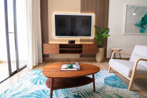 A modern living room with a flat-screen TV, wooden furniture, a potted plant, and a sofa. - 2-bedroom apartment in lovely Punta Cana with AC and gym access (Punta Cana)