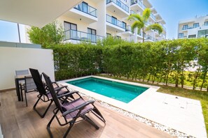 Zona de piscina exterior moderna amb gandules i vista d'un edifici residencial al fons.