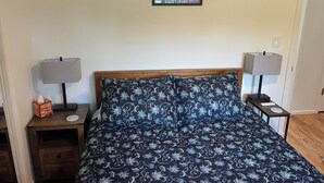 A bedroom with a wooden bed, two bedside tables with lamps, a framed picture on the wall, and a box of tissues on the left table. - Awesome Little House ! (Mountlake Terrace)