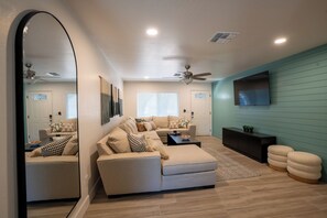 A living room with a large mirror, a sectional sofa, a coffee table, and a television on a wall.