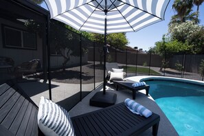 A poolside area with a covered seating area, a pool, and a fenced backyard.