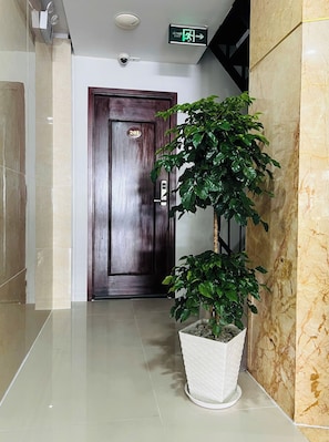 Un pasillo con piso de mármol, una planta en maceta, una puerta con placa de número y una señal de salida.