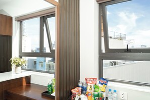 Habitación de hotel con dos ventanas amplias, un escritorio de madera y una variedad de aperitivos y bebidas sobre el alféizar.