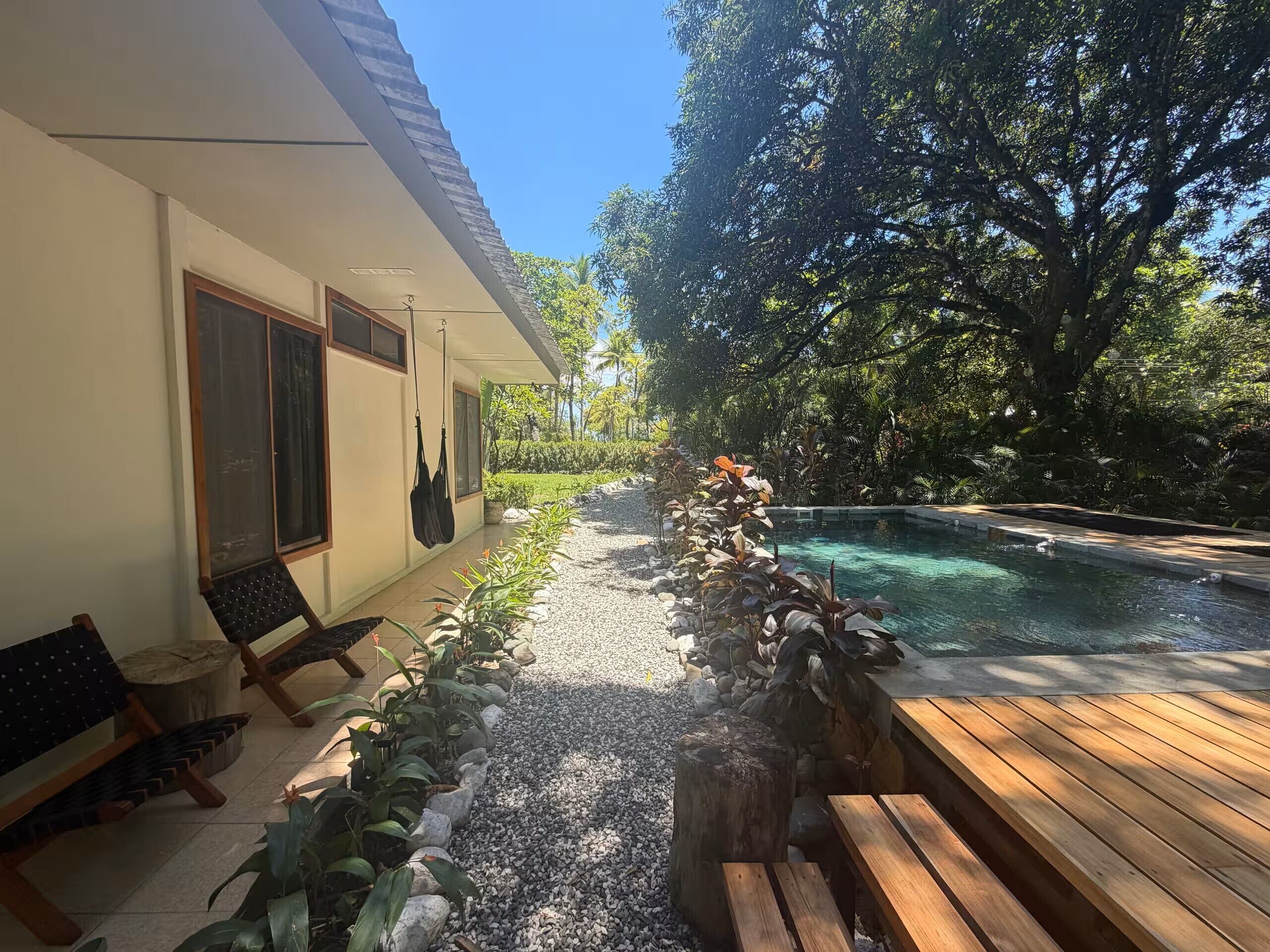 A pool area with a wooden deck, a stone pathway, and a variety of plants.