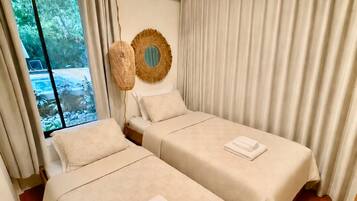 A hotel room with two beds, a large window, an air conditioning unit, and a view of greenery outside.
