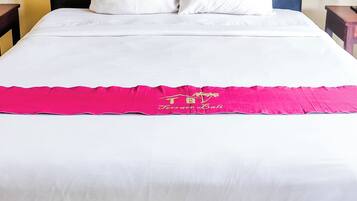 A bed with a black headboard, white bedding, and a pink decorative item.