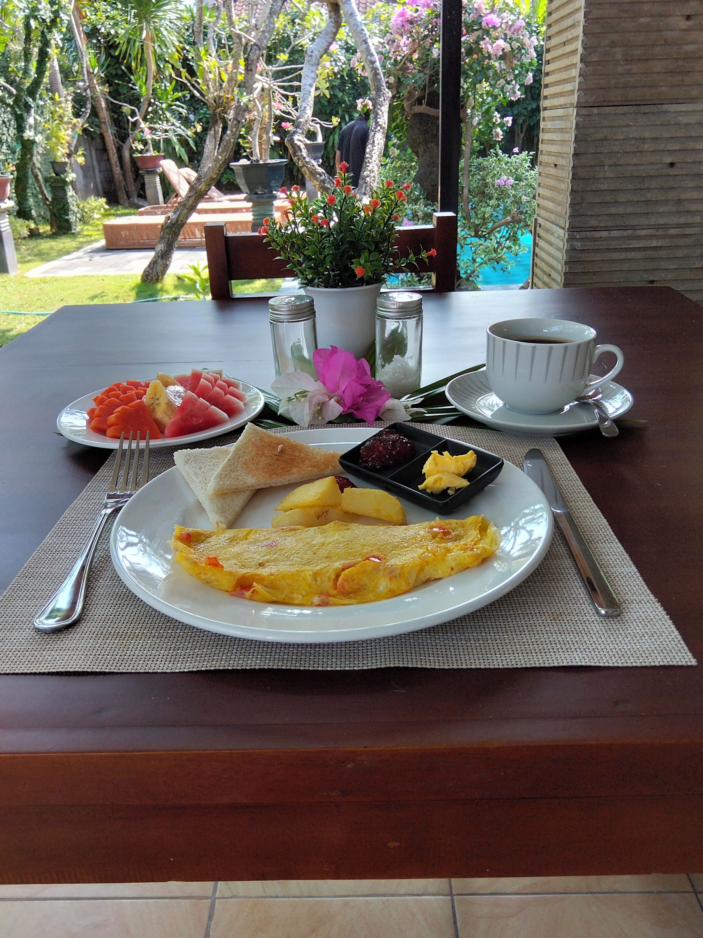 A breakfast setting with a plate of eggs, toast, fruit, and condiments on a table.