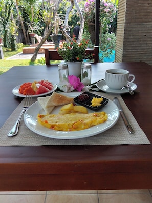 A breakfast setting with a plate of eggs, toast, fruit, and condiments on a table.