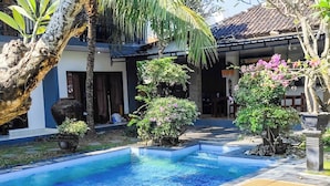 A pool area with lounge chairs, a palm tree, and a building with a tiled roof.