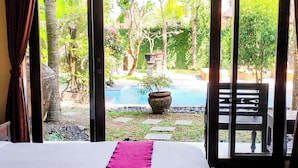 A hotel room with a bed, a view of a swimming pool, and a patio area.