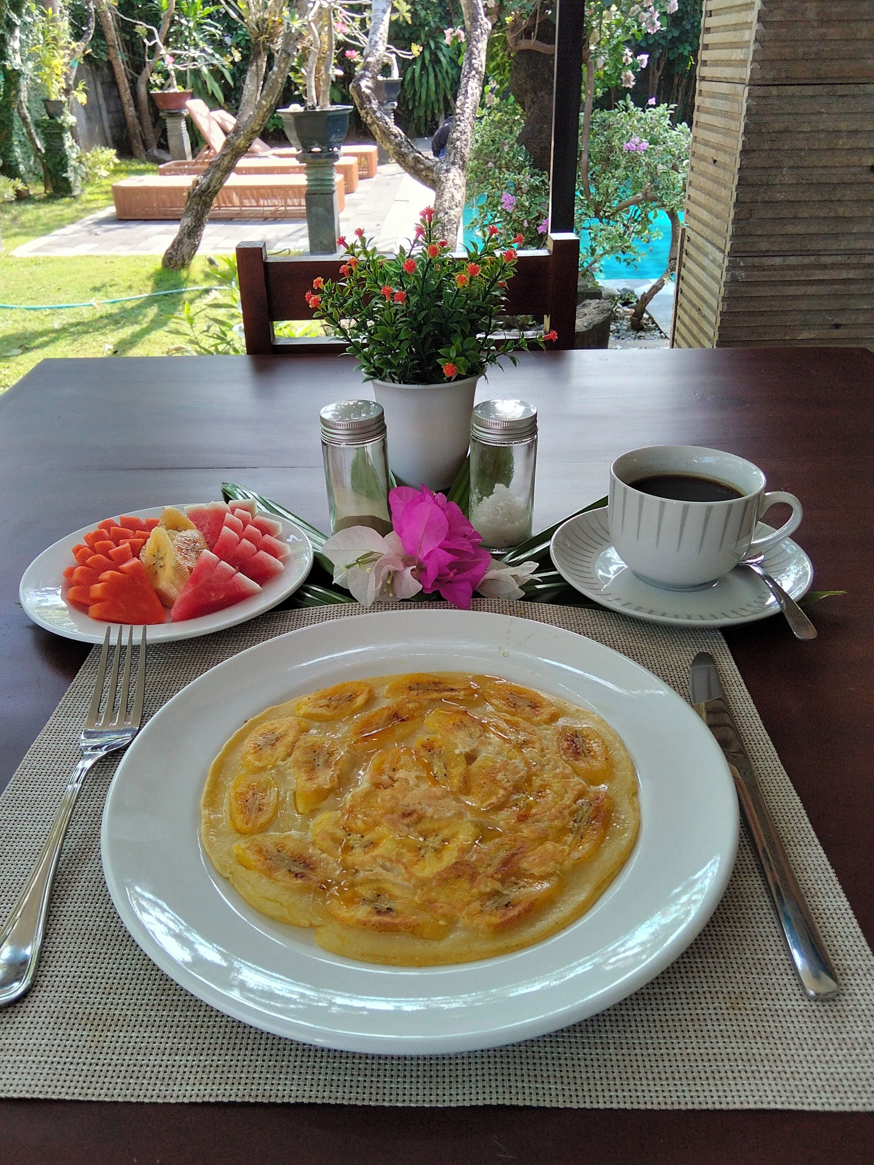 Una mesa con un plato de comida, una taza de café y una flor.