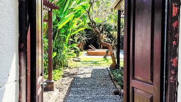 Un umbral abierto que da a un jardín con un camino de grava, plantas en macetas y un banco de madera.