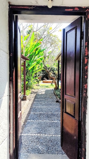An open doorway leading to a garden with a gravel path, potted plants, and a wooden bench.