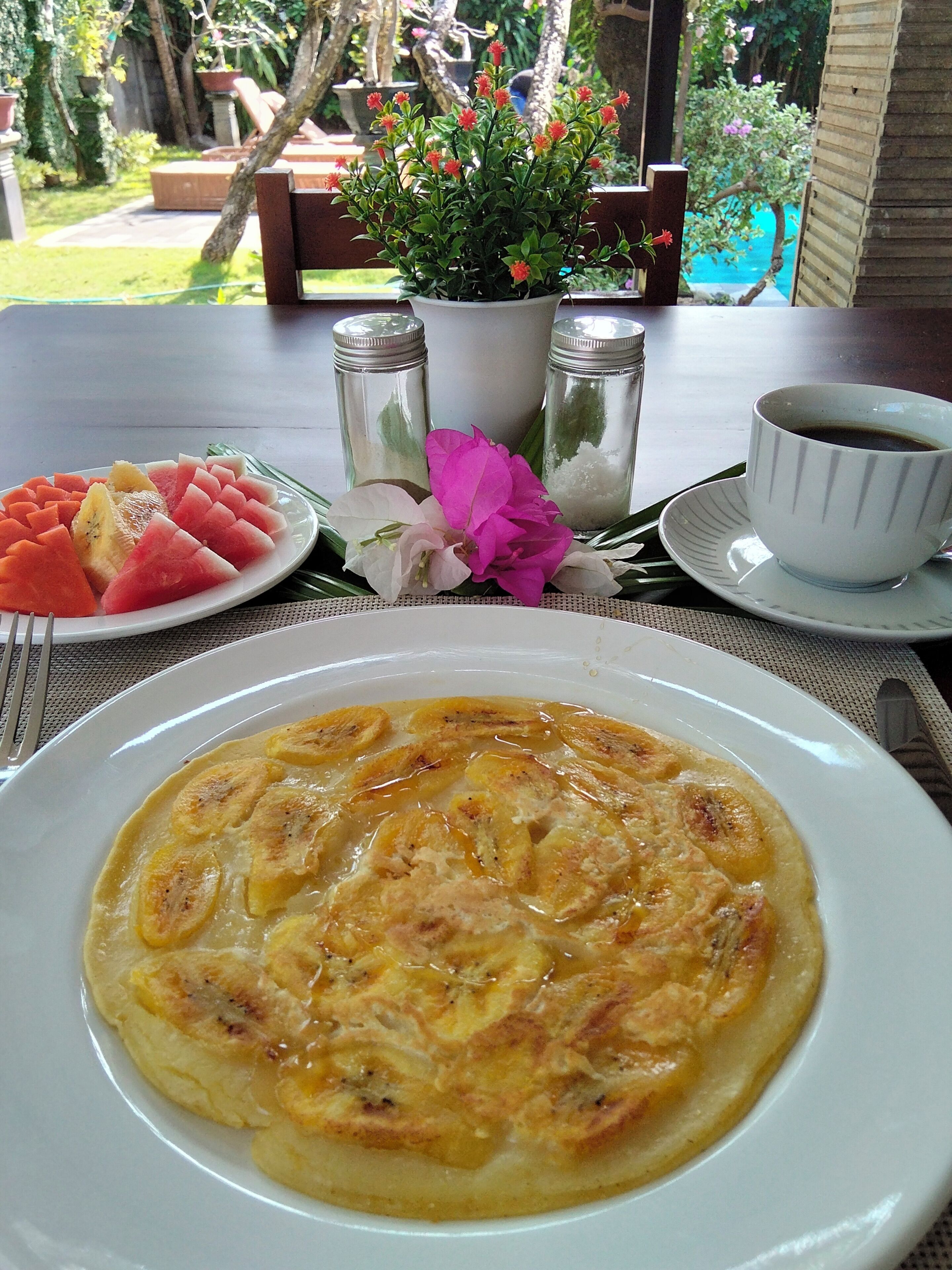 Una mesa de comedor con un plato de rodajas de plátano, una taza de café y una planta en maceta.