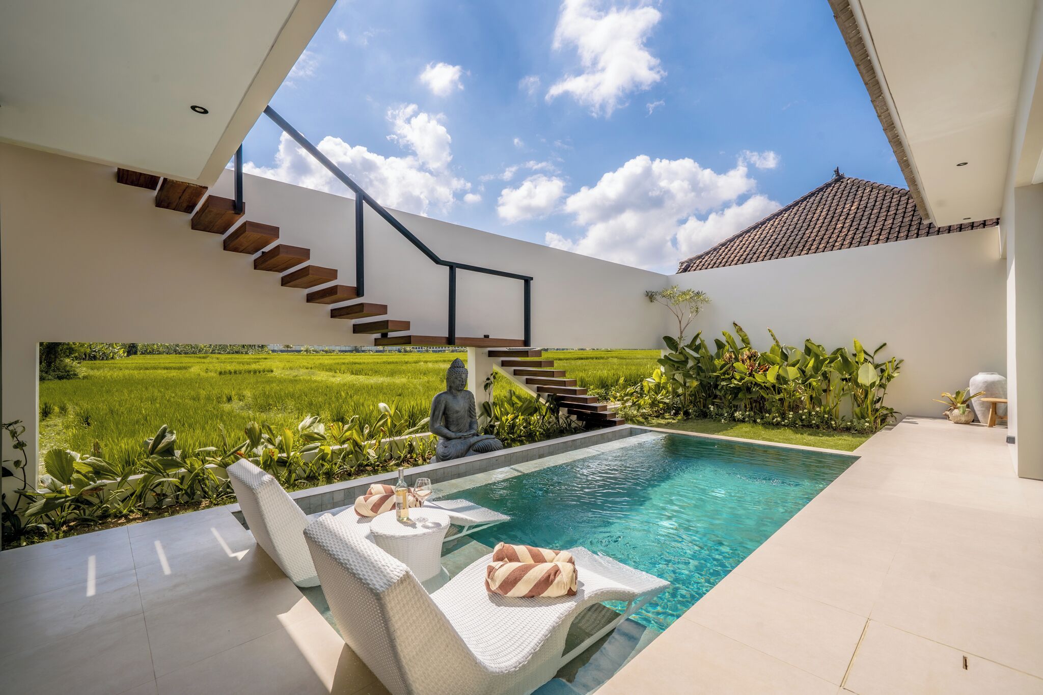 A modern pool area with a clear view of a lush green field, a staircase, and a Buddha statue.