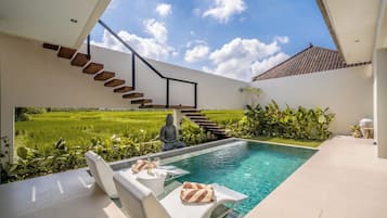 A modern pool area with a clear view of a lush green field, a staircase, and a Buddha statue.