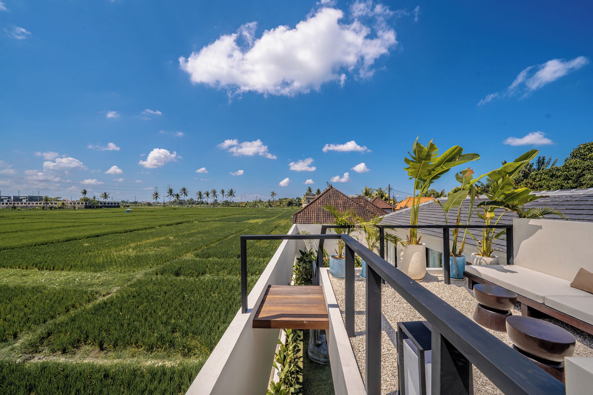 Um terraço com vista para um campo verde, um edifício com telhado de cerâmica e uma área de estar com mesa e cadeiras.