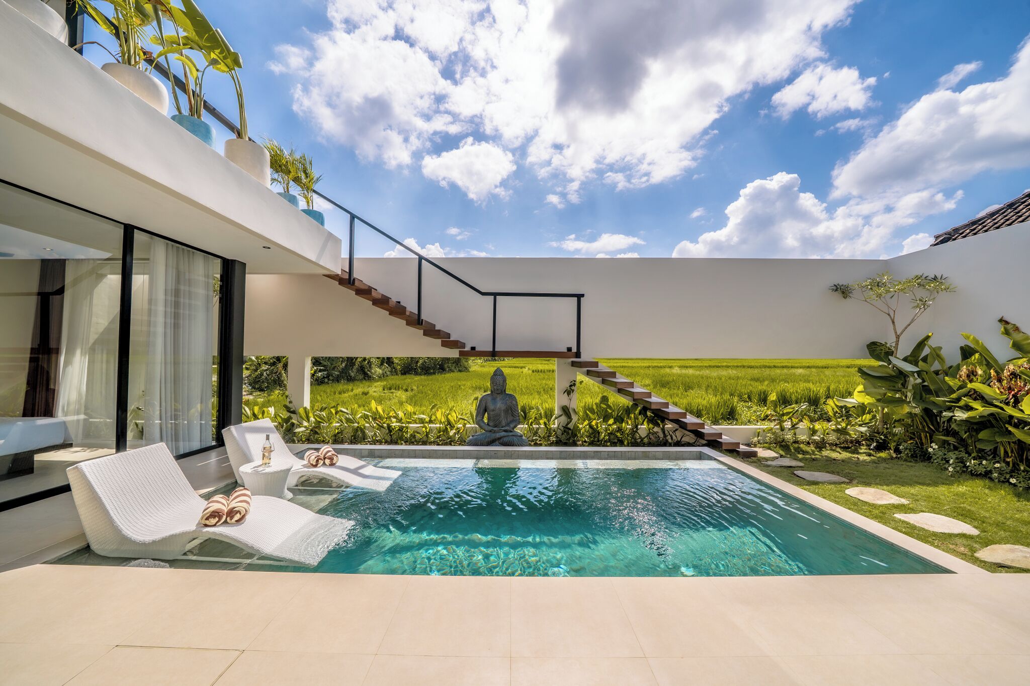 Una casa moderna con piscina, una estatua de Buda y una escalera que lleva a un balcón.