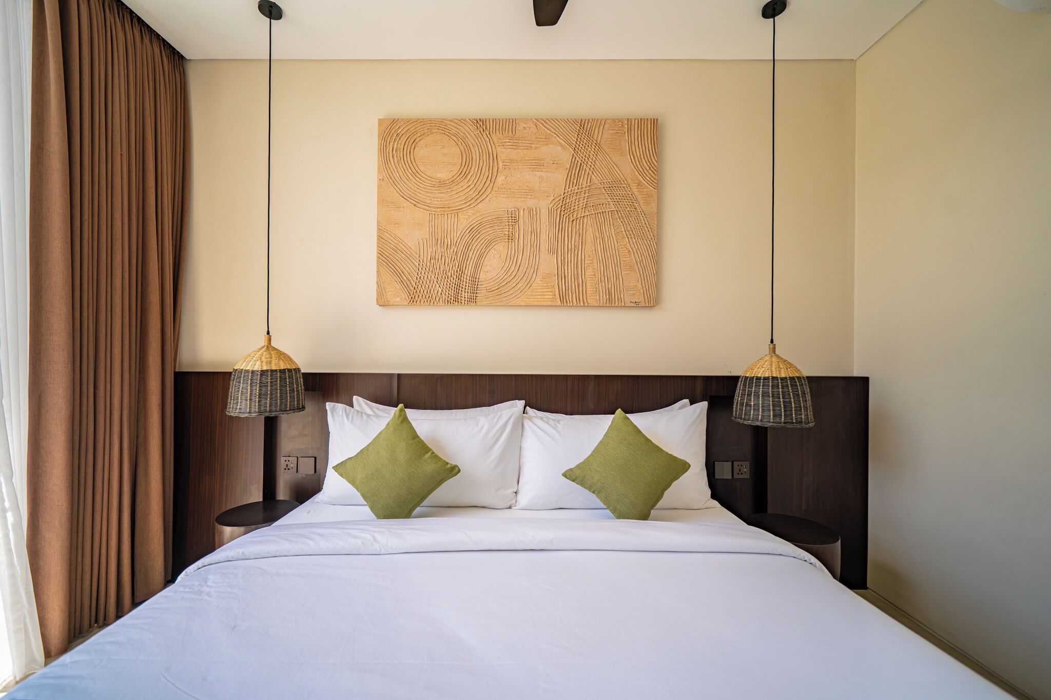 Habitación de hotel con una cama grande, dos mesitas de noche, un cabecero con diseño texturizado y dos lámparas colgantes.