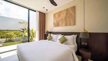 A hotel room with a large bed, a view of a green landscape, a ceiling fan, and a wall-mounted artwork.