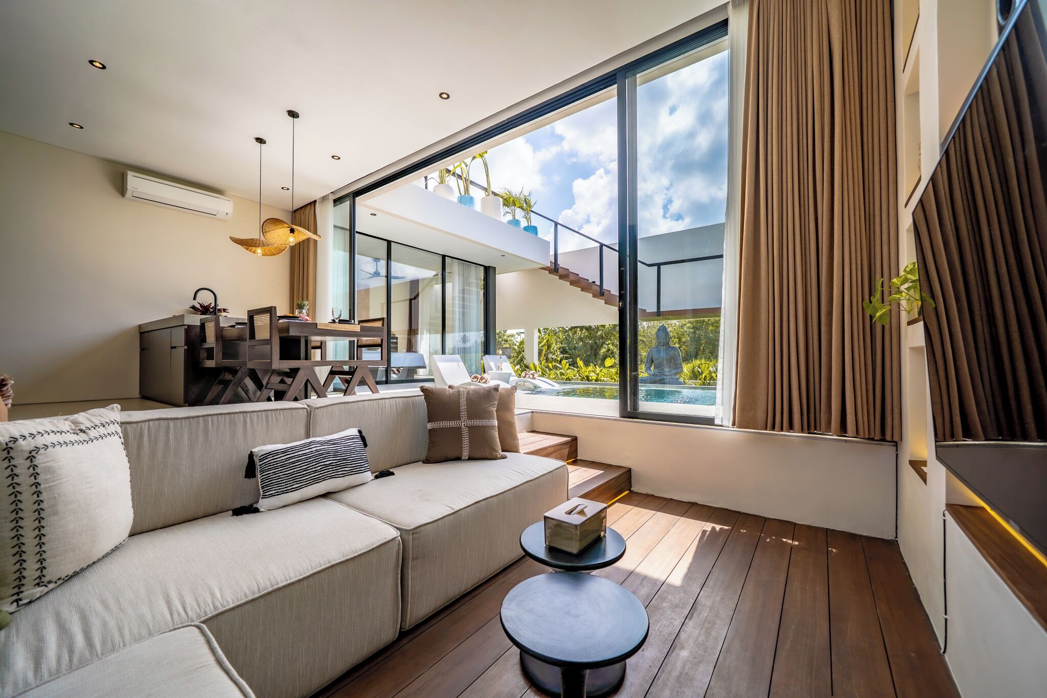 A modern living room with a large window, a sofa, a dining table, and a staircase leading to an outdoor area.