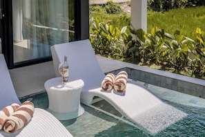Un área junto a la piscina con sillones, una botella de vino y toallas.