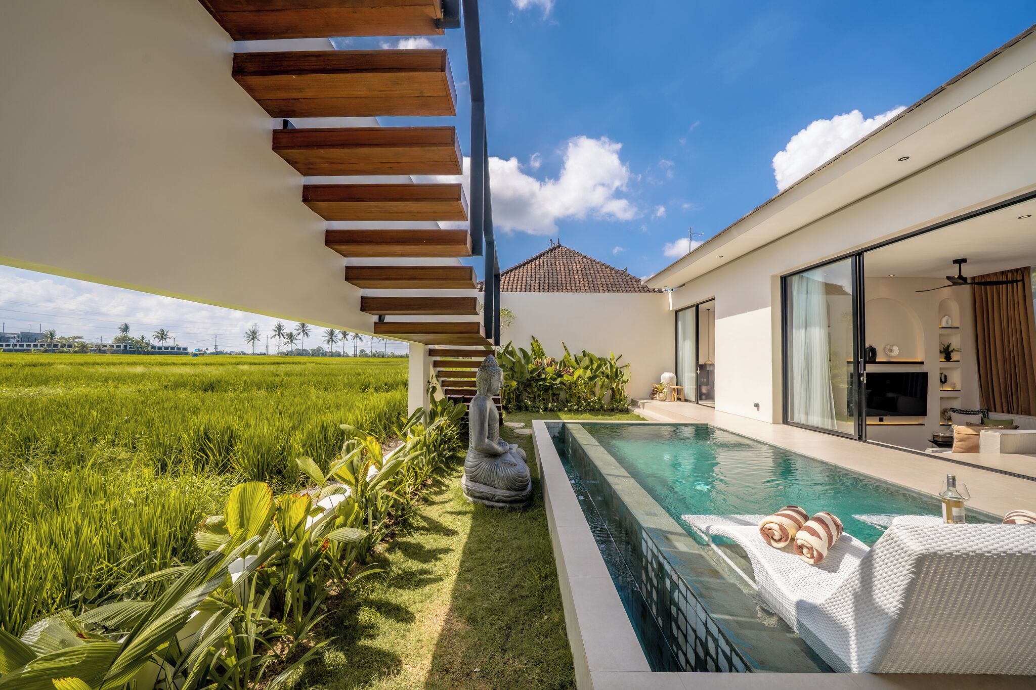 A modern house with a swimming pool, a wooden staircase, and a view of a green field.
