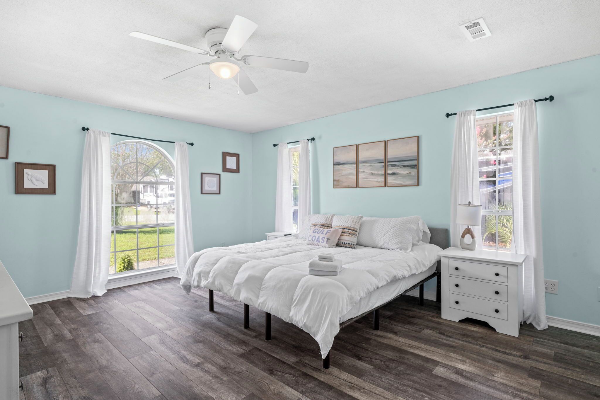 A bedroom with a bed, a nightstand, a ceiling fan, and a window with curtains.
