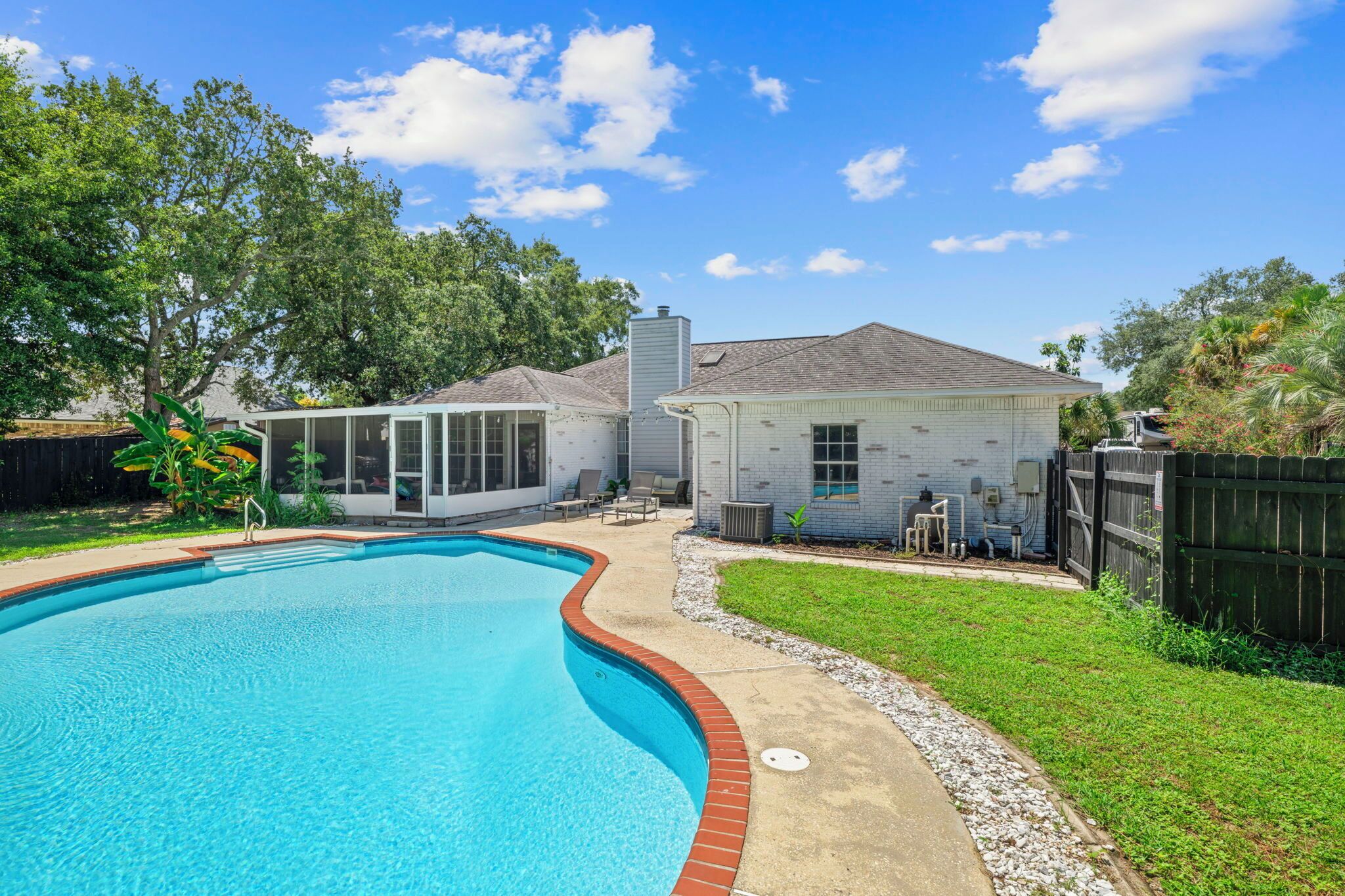 A backyard with a swimming pool, a covered patio, and a small house.