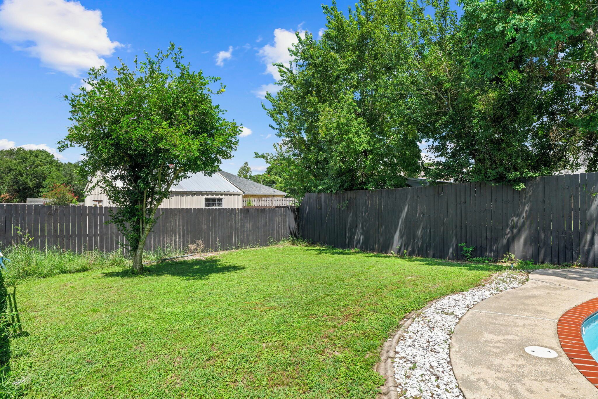 A backyard with a wooden fence, a grassy lawn, and a house with a metal roof.