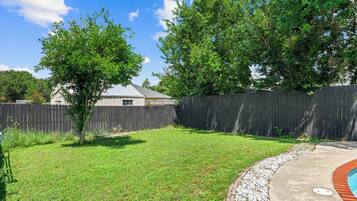 A backyard with a wooden fence, a grassy lawn, and a house with a metal roof.