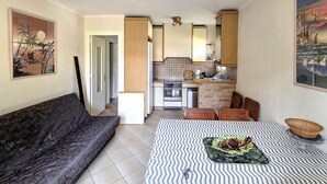 Ein gemütlicher Wohnraum mit Sofa, Esstisch mit einem gemusterten Tischläufer, Küchenzeile mit Herd und Schränken sowie Bildern an den Wänden.