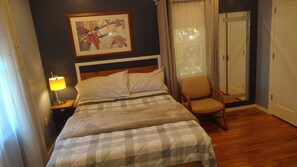 A hotel room with a bed, a chair, a nightstand with a lamp, a framed picture on the wall, and a door.