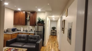 A compact kitchen with wooden cabinets, a refrigerator, and a microwave. A leather sofa is positioned in the foreground.