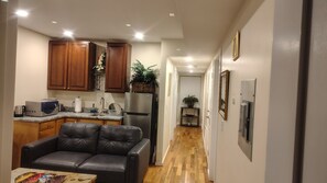 A compact kitchen with wooden cabinets, a refrigerator, and a microwave. A leather sofa is positioned in the foreground.