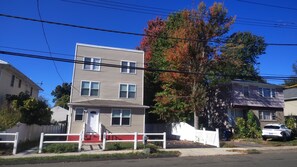 A two-story residential building with a front porch, a mailbox, and a street view.