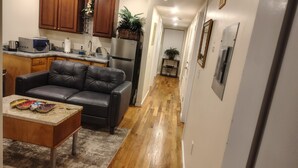 A compact kitchen with a refrigerator, microwave, and coffee maker. A leather sofa and a small table with decorative plates are in the living area.